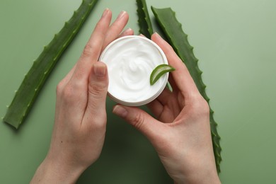 Woman with moisturizing cream and aloe vera leaves on green background, top view