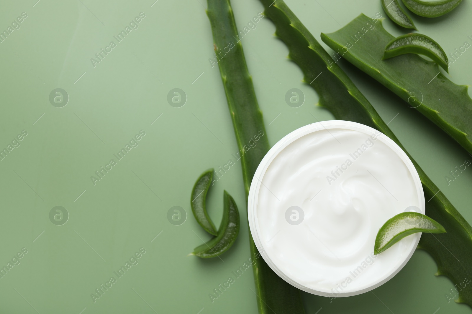 Photo of Moisturizing cream with extract of aloe vera in jar and cut leaves on green background, flat lay. Space for text