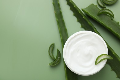 Moisturizing cream with extract of aloe vera in jar and cut leaves on green background, flat lay. Space for text