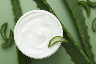 Photo of Moisturizing cream with extract of aloe vera in jar and cut leaves on green background, flat lay