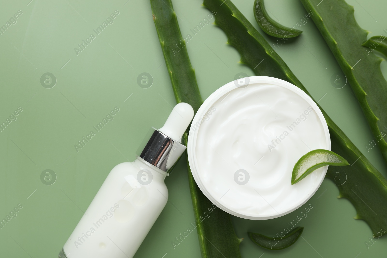 Photo of Moisturizing cream with extract of aloe vera in jar, serum and cut leaves on green background, flat lay. Space for text