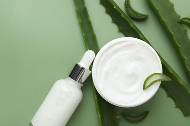 Moisturizing cream with extract of aloe vera in jar, serum and cut leaves on green background, flat lay. Space for text