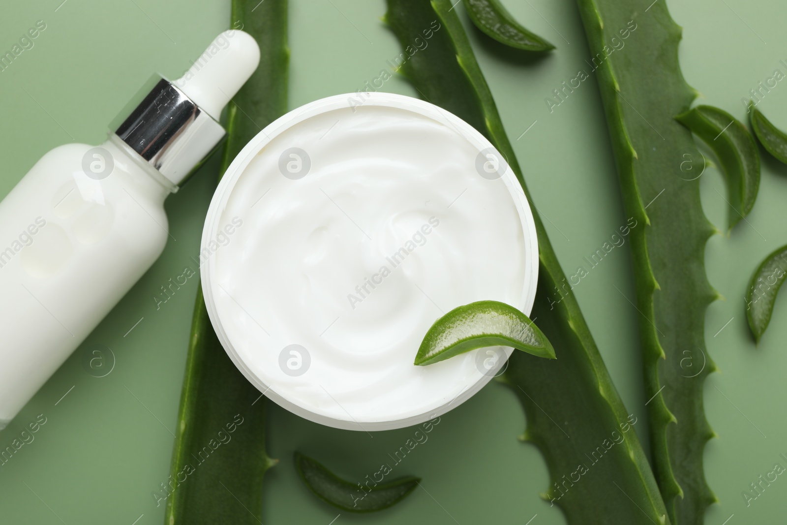 Photo of Moisturizing cream with extract of aloe vera in jar, serum and cut leaves on green background, flat lay