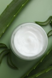 Photo of Moisturizing cream with extract of aloe vera in jar and cut leaves on green background, flat lay