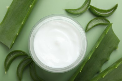 Photo of Moisturizing cream with extract of aloe vera in jar and cut leaves on green background, flat lay