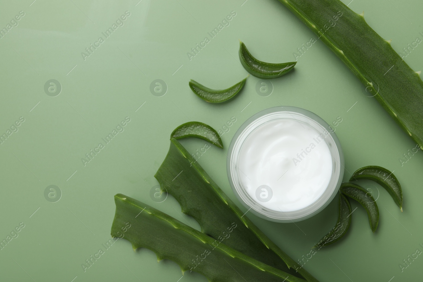 Photo of Moisturizing cream with extract of aloe vera in jar and cut leaves on green background, flat lay. Space for text