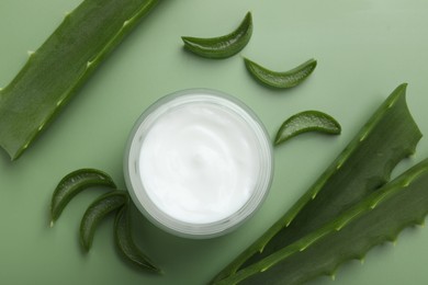 Moisturizing cream with extract of aloe vera in jar and cut leaves on green background, flat lay