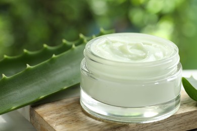 Moisturizing cream with extract of aloe vera in jar and cut leaves on white table against blurred green background, closeup