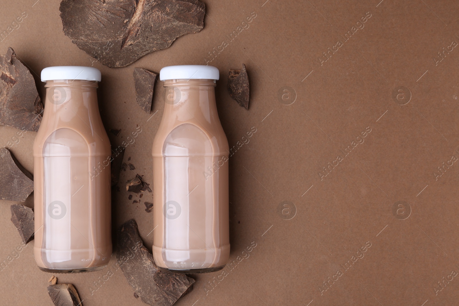 Tasty chocolate milk in glass bottles and pieces of chocolate on brown background, flat lay. Space for text Photo of Tasty chocolate milk in glass bottles and pieces of chocolate on brown background, flat lay. Space for text