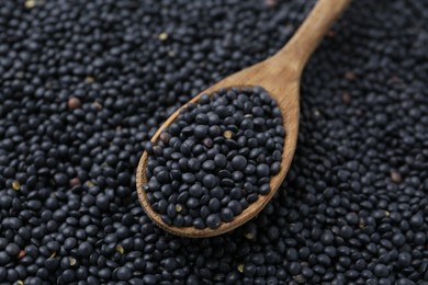 Photo of Raw black lentils and spoon as background, closeup view