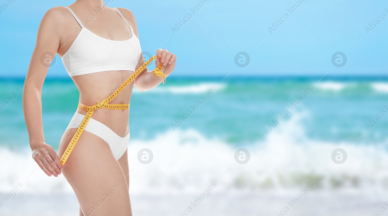 Image of Get fit for summer. Woman with measuring tape showing her slim body on beach, closeup. Banner design with space for text