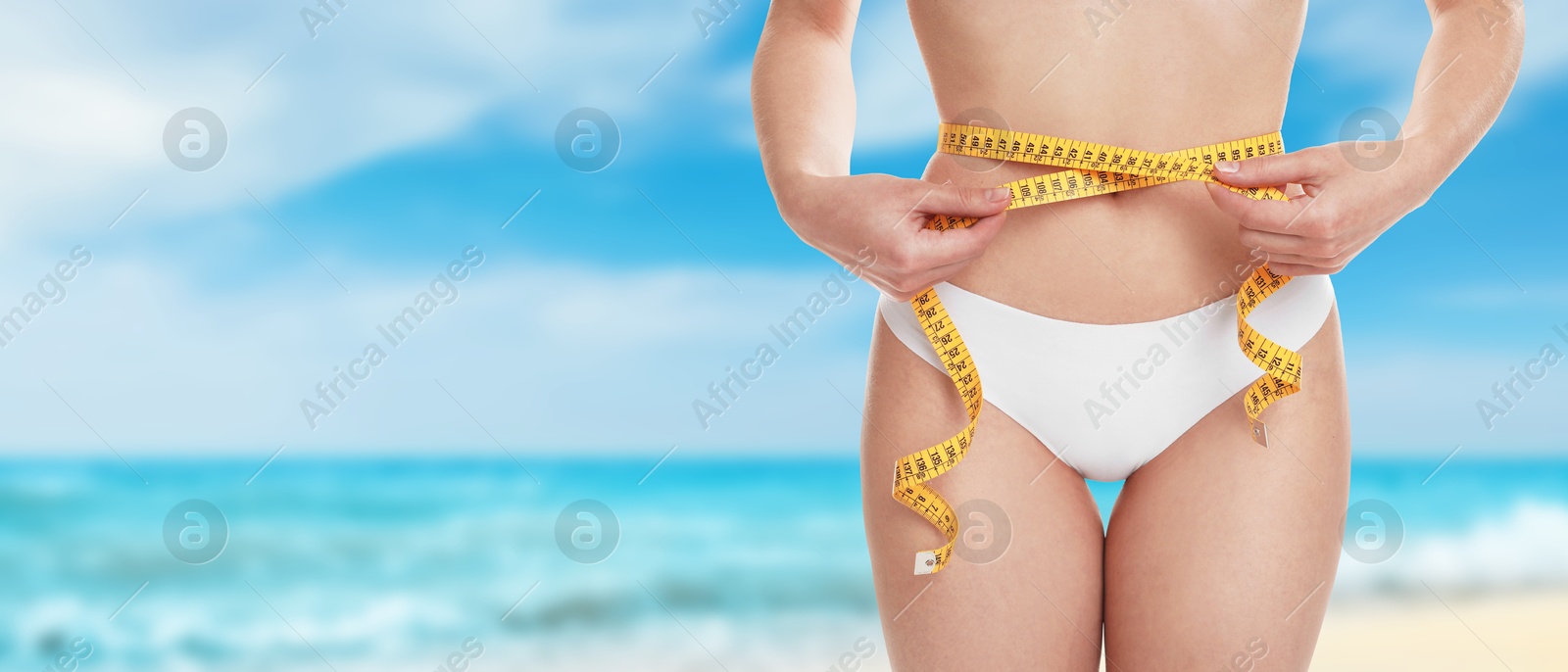 Image of Get fit for summer. Woman with measuring tape showing her slim body on beach, closeup. Banner design with space for text