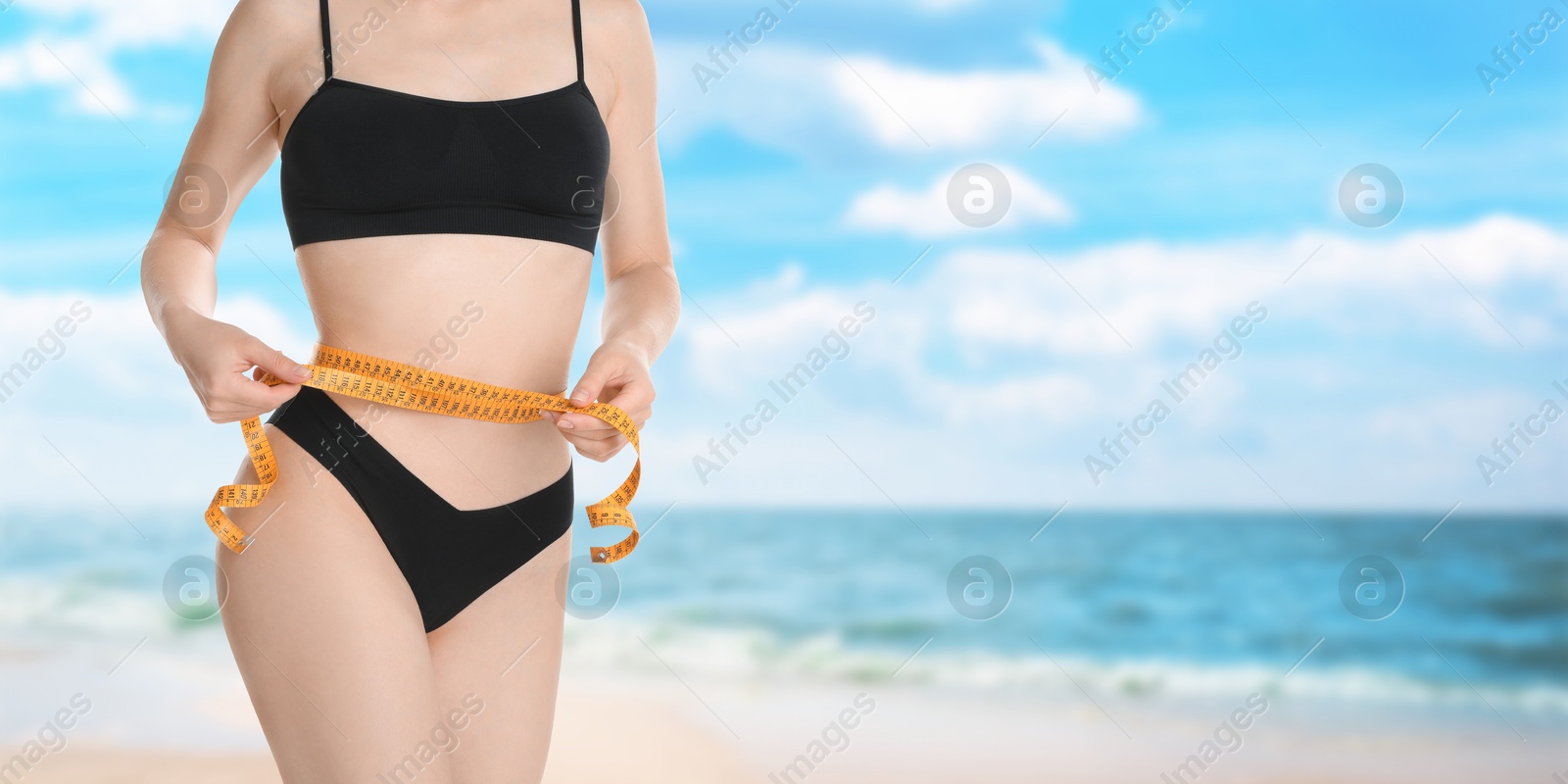 Image of Get fit for summer. Woman with measuring tape showing her slim body on beach, closeup. Banner design with space for text