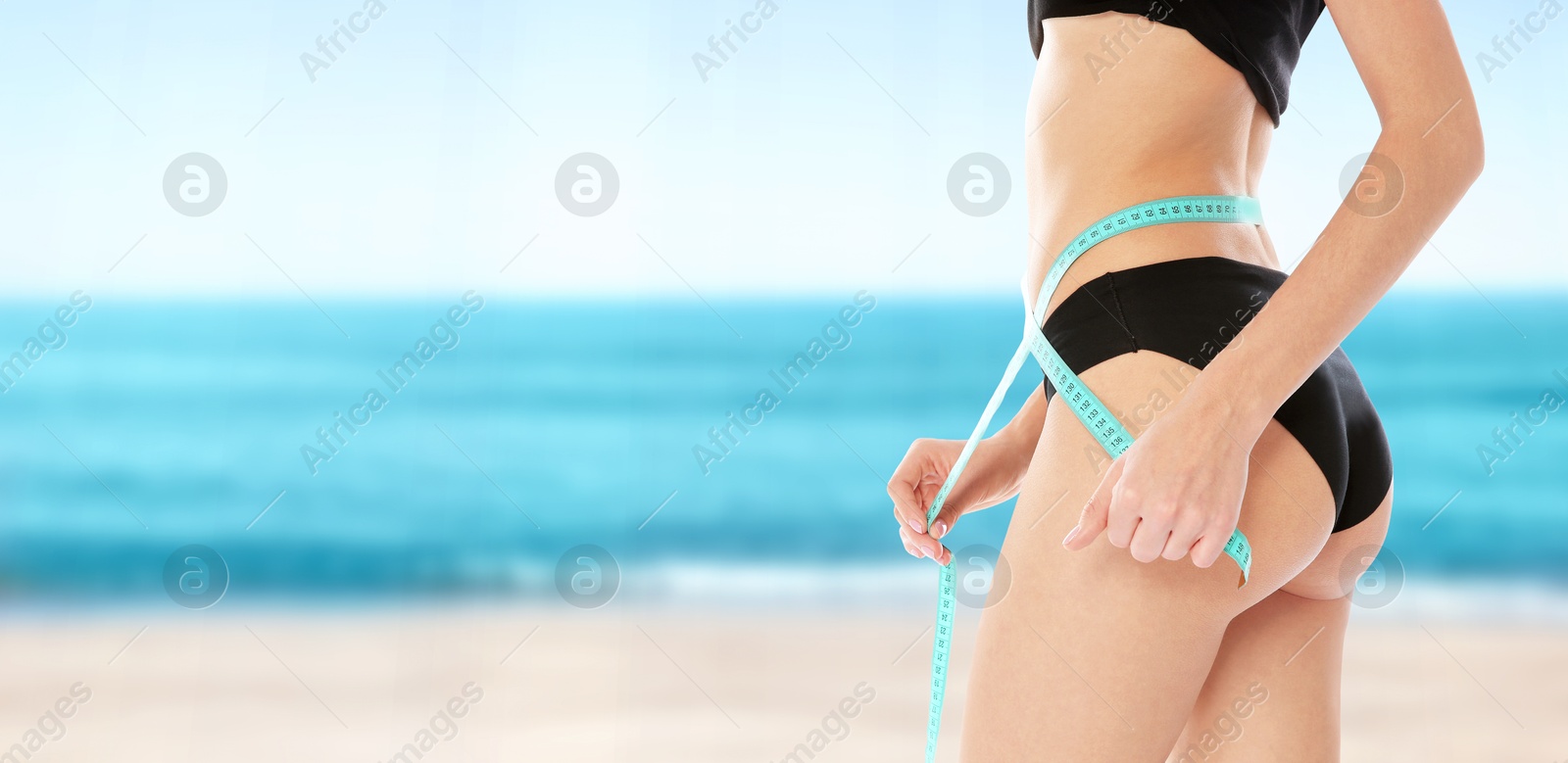 Image of Get fit for summer. Woman with measuring tape showing her slim body on beach, closeup. Banner design with space for text