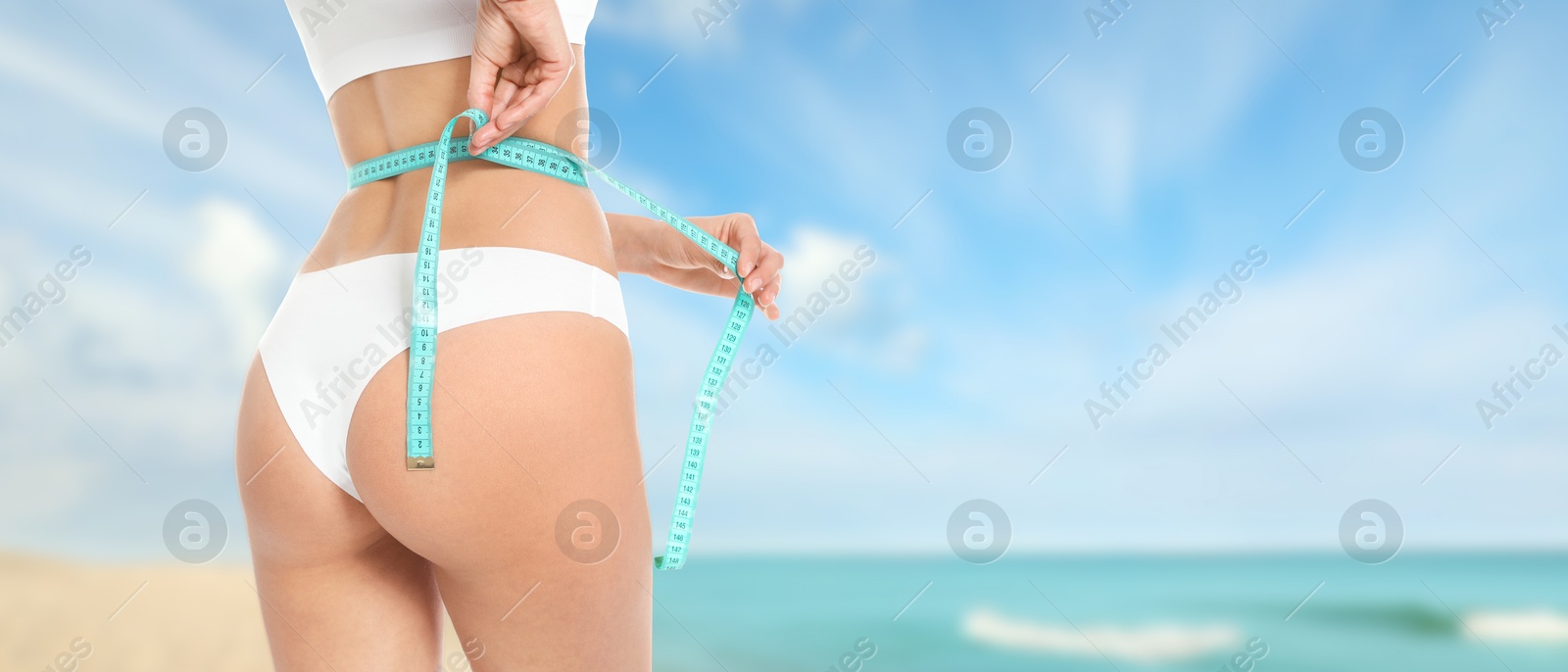 Image of Get fit for summer. Woman with measuring tape showing her slim body on beach, closeup. Banner design with space for text