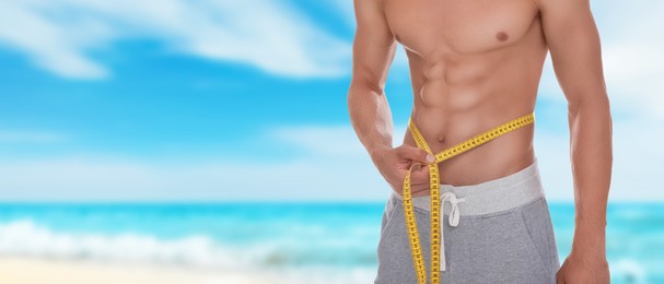 Image of Man with measuring tape showing his athletic body on beach, closeup. Banner design with space for text. Motivation to get fit for summer