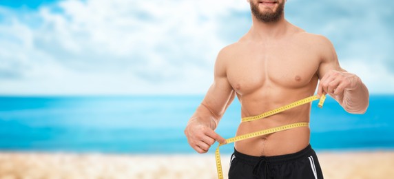 Image of Man with measuring tape showing his athletic body on beach, closeup. Banner design with space for text. Motivation to get fit for summer