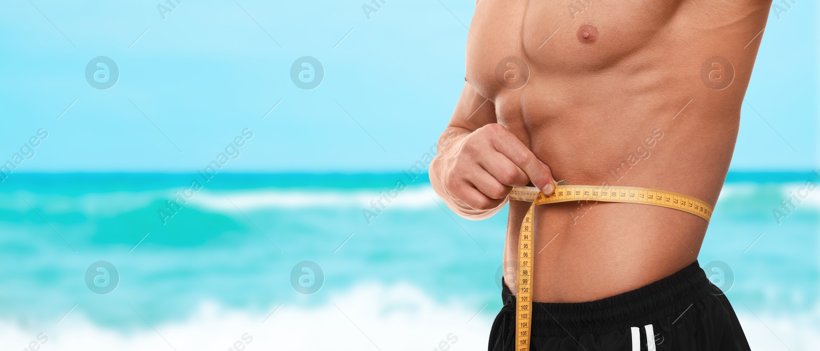 Image of Man with measuring tape showing his athletic body on beach, closeup. Banner design with space for text. Motivation to get fit for summer