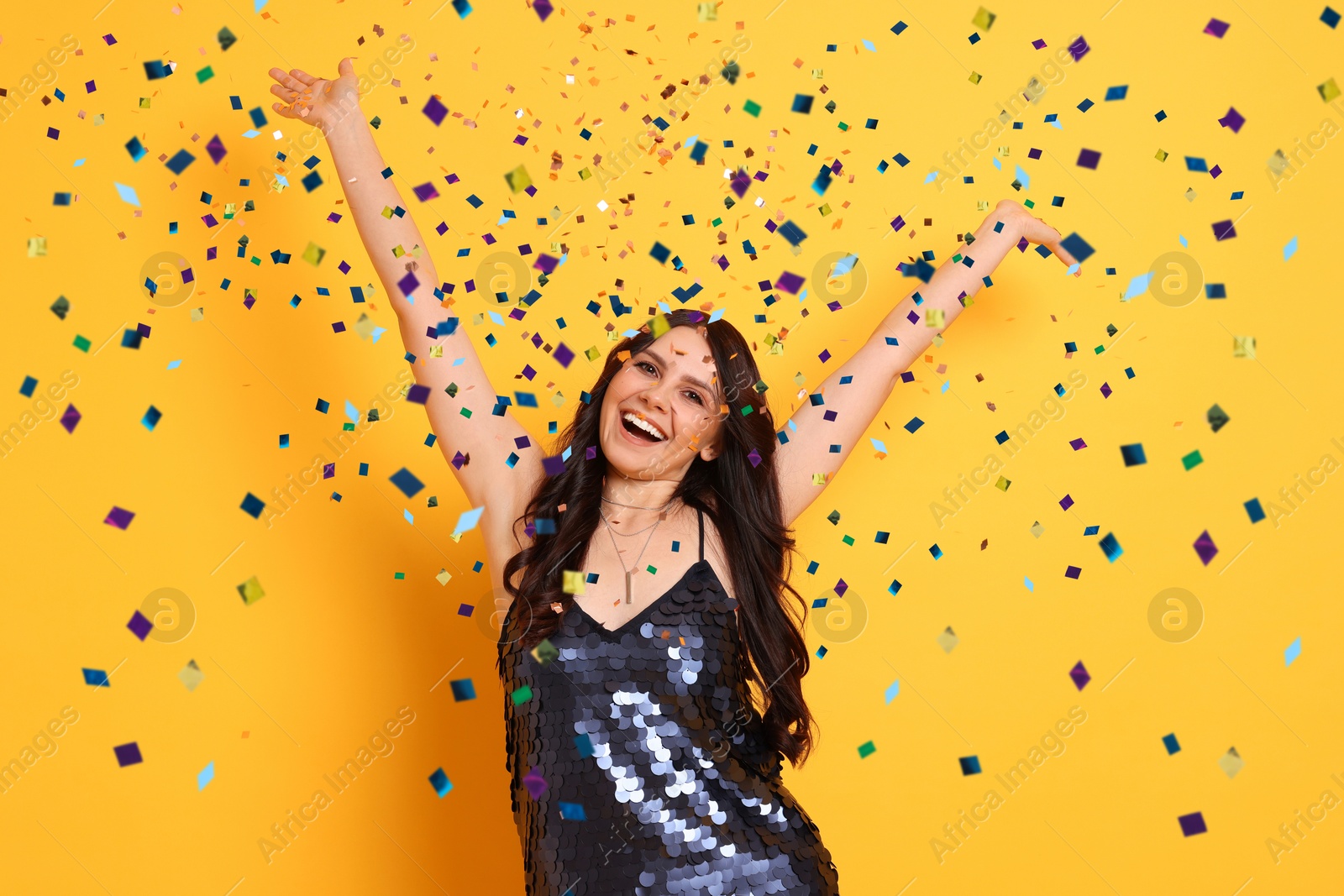 Image of Happy woman under falling confetti on orange background. Surprise party