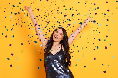 Image of Happy woman under falling confetti on orange background. Surprise party