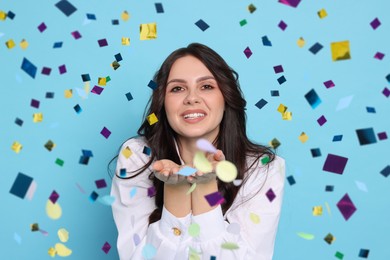 Image of Happy woman under falling confetti on light blue background. Surprise party