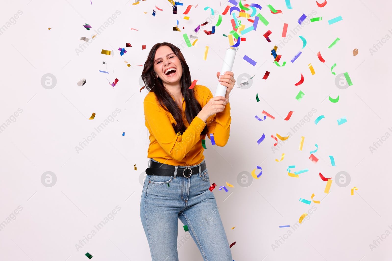 Image of Happy woman blowing up confetti popper on light background. Surprise party