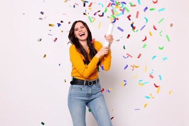 Happy woman blowing up confetti popper on light background. Surprise party