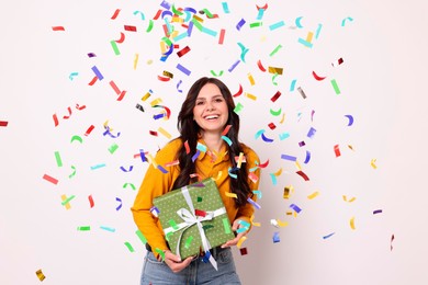 Image of Happy woman with gift under falling confetti on light background. Surprise party