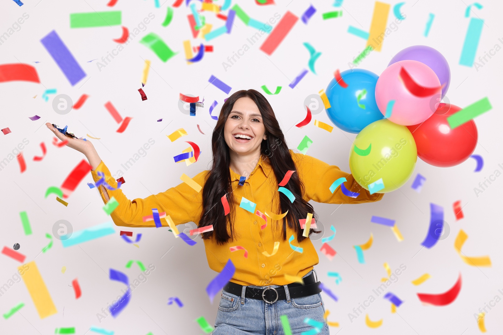 Image of Happy woman with balloons under falling confetti on light background. Surprise party