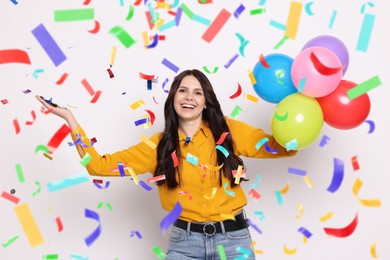 Happy woman with balloons under falling confetti on light background. Surprise party