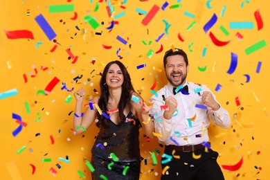 Image of Happy woman and man under falling confetti on orange background. Surprise party