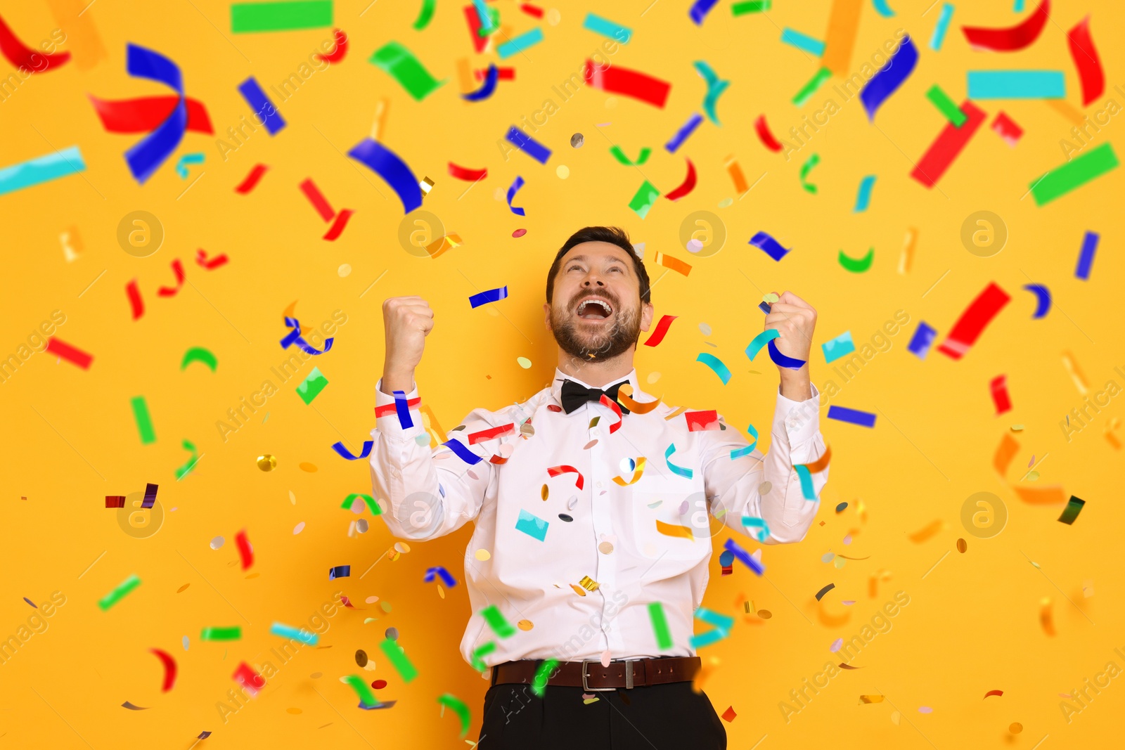 Image of Happy man under falling confetti on orange background. Surprise party