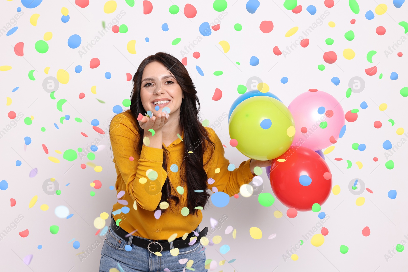 Image of Happy woman with balloons under falling confetti on light background. Surprise party