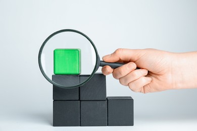 Woman with magnifying glass exploring stairs made of different cubes on white background, closeup. Search concept