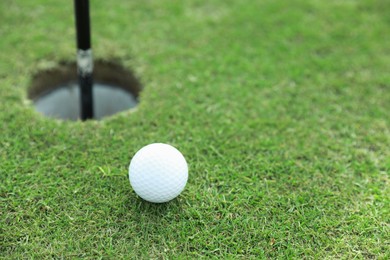 Golf ball near hole on green course, space for text