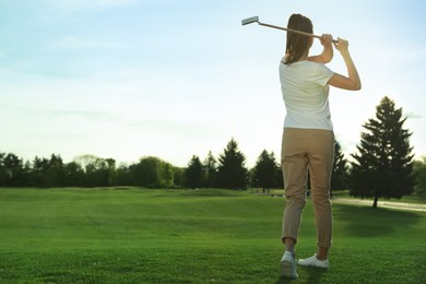 Woman playing golf on green course, back view. Space for text