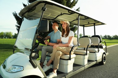 Happy couple driving golf cart on road in park