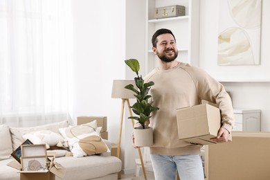 Photo of Moving day. Man with cardboard box and houseplant in his new home