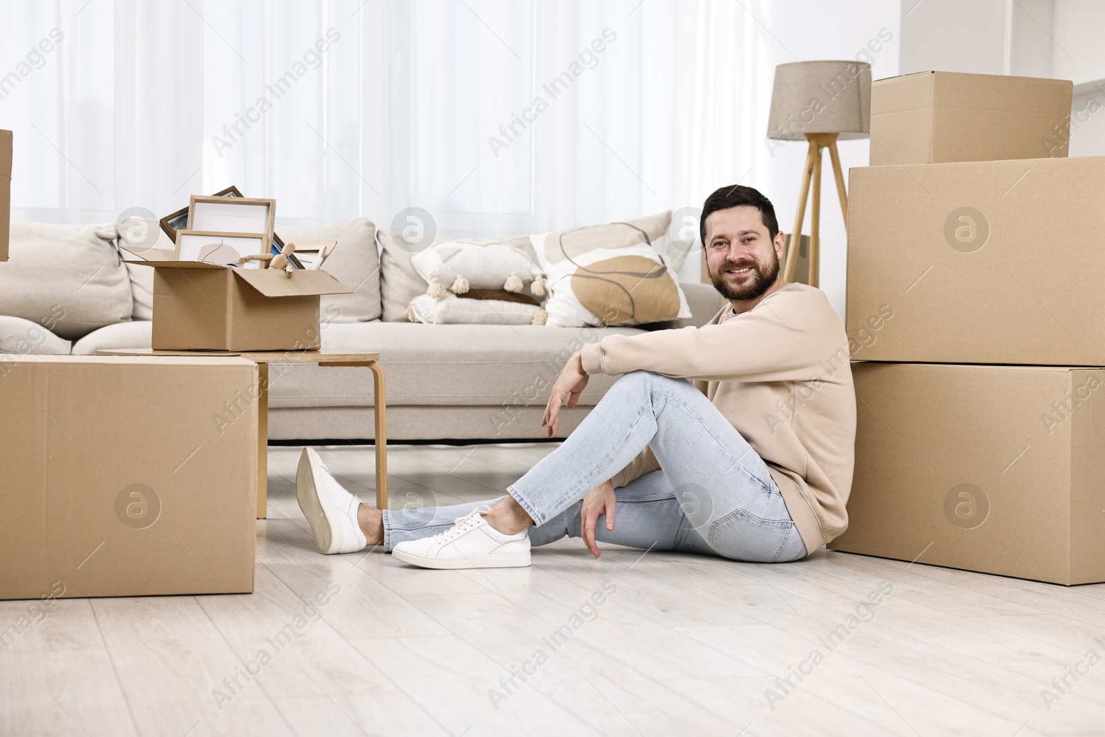 Photo of Moving day. Man resting on floor near cardboard boxes in his new home