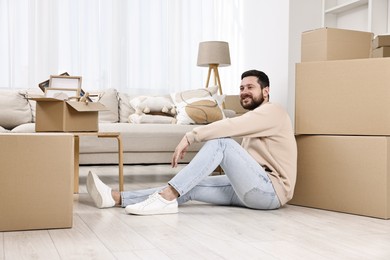 Moving day. Man resting on floor near cardboard boxes in his new home