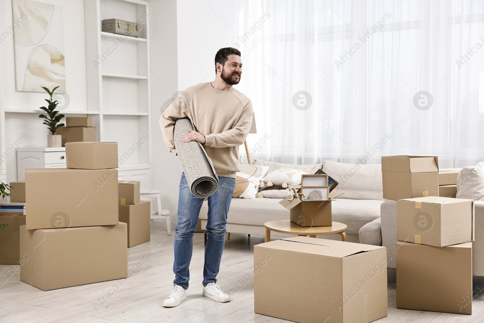 Photo of Moving day. Happy man with rug in his new home