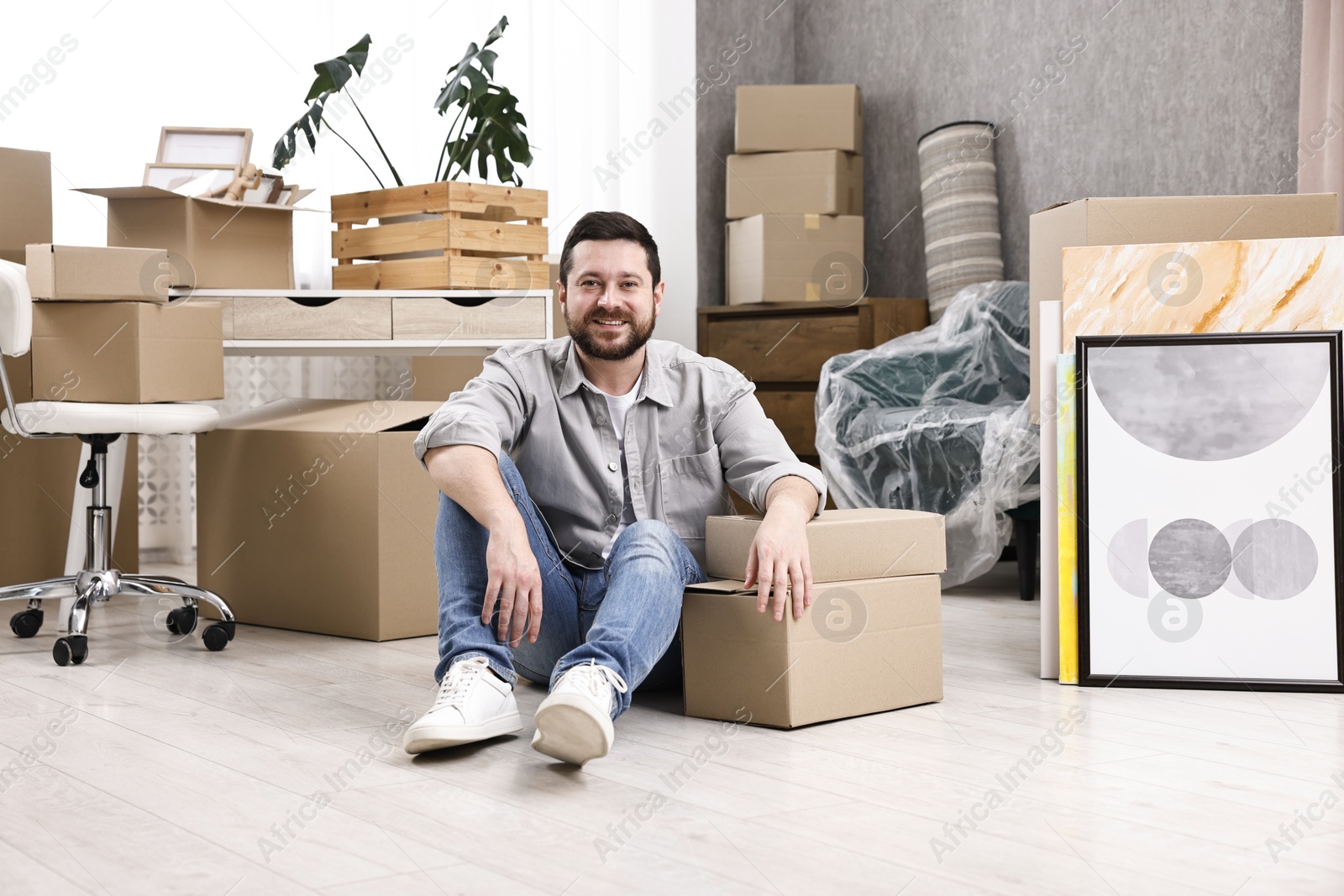 Photo of Moving day. Man resting on floor near cardboard boxes in his new home