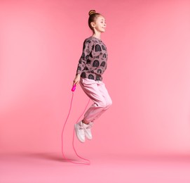 Photo of Cute little girl with jump rope on light pink background