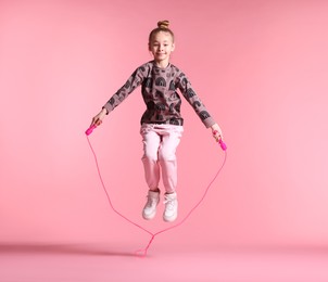 Cute little girl with jump rope on light pink background