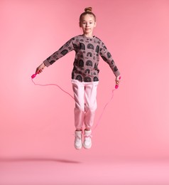 Cute little girl with jump rope on light pink background