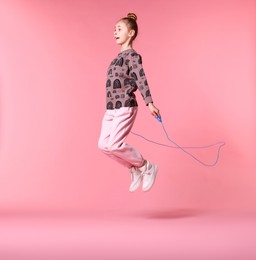 Cute little girl with jump rope on light pink background