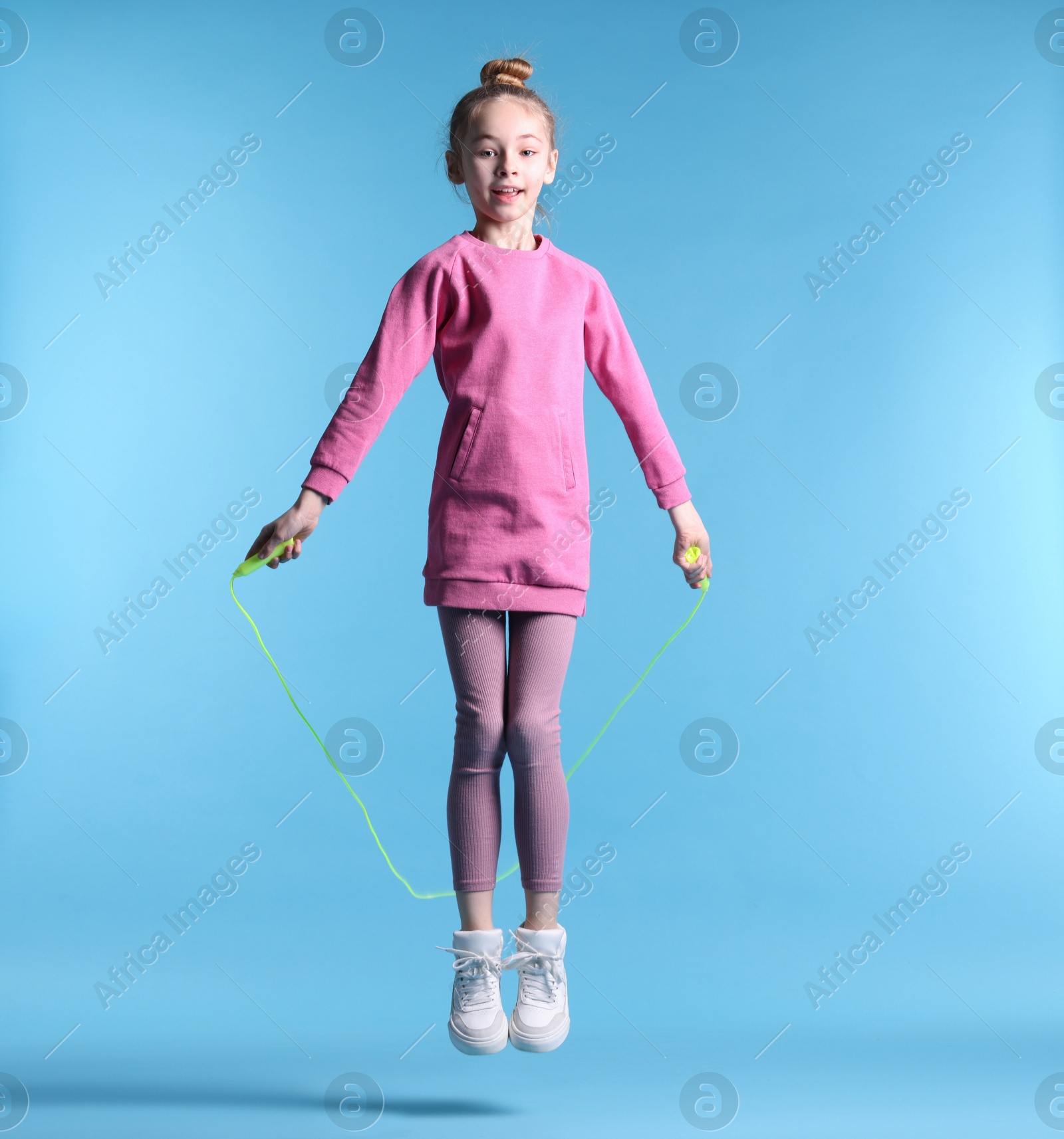 Photo of Cute little girl with jump rope on light blue background