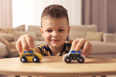 Photo of Little boy playing with toy cars at wooden table indoors