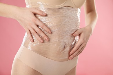 Photo of Woman doing spa body wraps on her belly against pink background, closeup