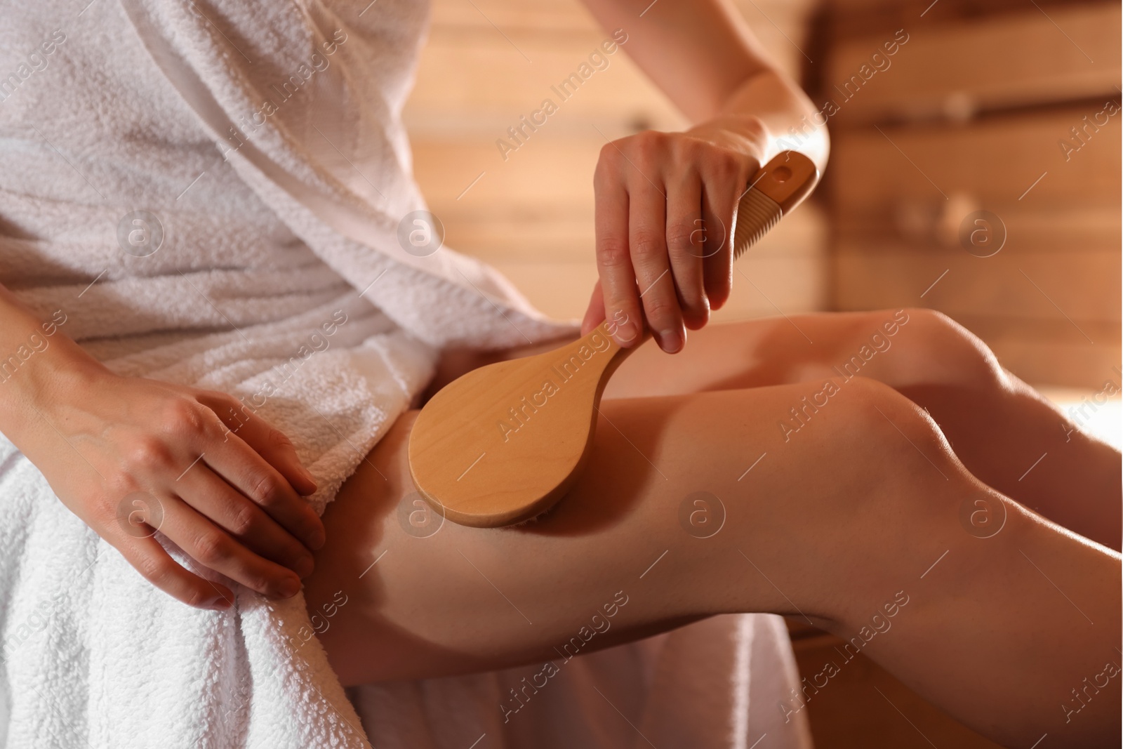 Photo of Woman massaging her leg with brush at sauna, closeup